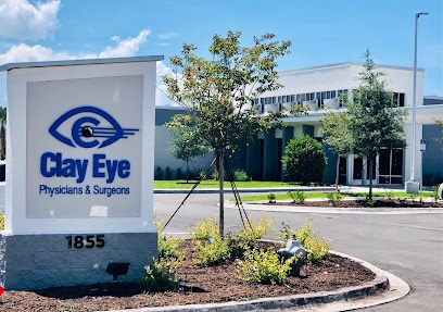 Eye Doctor in Fleming Island, FL 1 A large sign reading "Clay Eye Physicians & Surgeons" stands in front of a modern medical building on Fleming Island, surrounded by trees and landscaped plants beneath a blue sky. The address "1855" appears on the sign's base. - Claye Eye Physicians & Surgeons - the best eye surgeons in Jacksonville, Florida